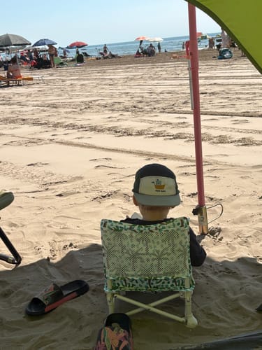 A customer's child sits in the patterned Kai baby chair on a sunny beach.