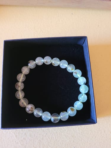 Photo d'avis d'un client montrant le bracelet Préhnite aux perles vert clair transparentes avec des touches noires, dans son écrin.
