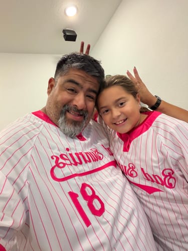Reviewer and a child smiling while wearing matching white and pink pinstriped custom baseball jerseys.