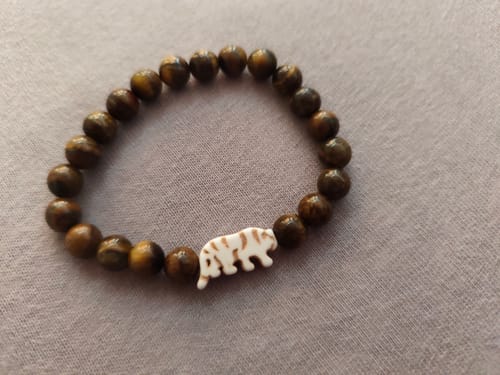 Customer's Prowl Bracelet with brown beads and a white tiger charm on a grey surface.