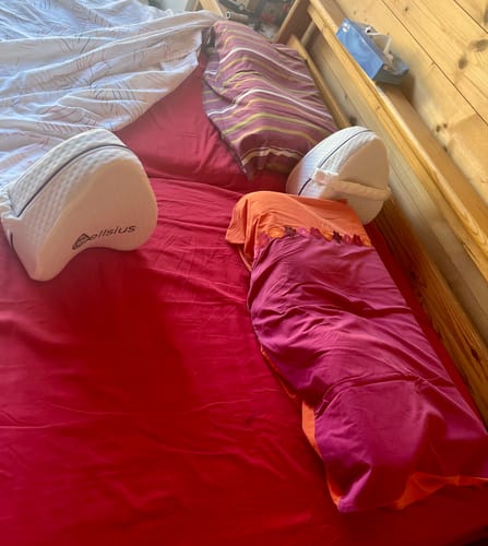 Un client montre le coussin de genou et le coussin papillon Cellsius sur un lit aux draps rouges.
