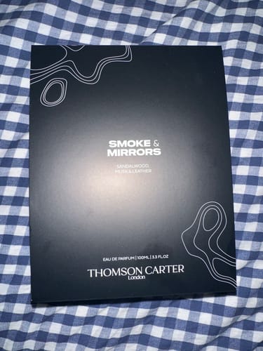 Customer's black box for Smoke & Mirrors Eau de Parfum resting on a checkered surface.