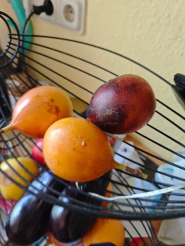 Ein Kunde zeigt mehrere orange und rötliche Granadillas in einem schwarzen Obstkorb.