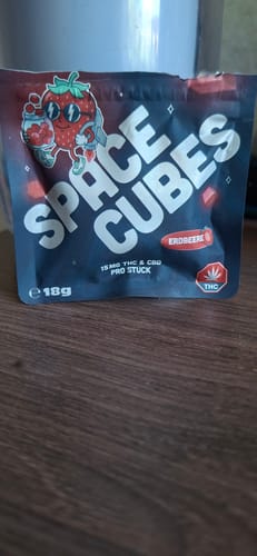 Kunde zeigt die schwarze Verpackung der Spacecubes mit Erdbeergeschmack auf einem Holztisch.