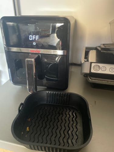 Customer's black Air Fryer Novio StonePro with the display off and the basket liner placed in front on a countertop.