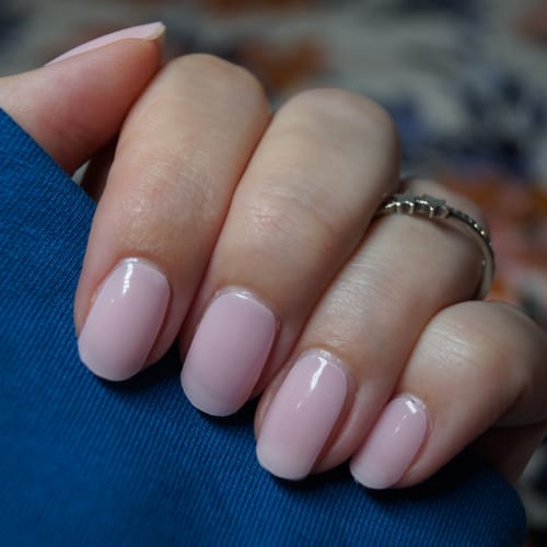 Hand einer Kundin, die die glänzenden, semi-transparenten UV-Gel-Nagelfolien Rosé Teint auf ihren Nägeln zeigt.