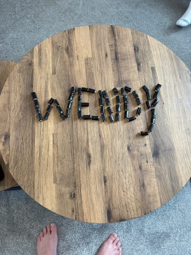 Customer using shiny black liquorice pieces to spell the name 'Wendy' on a wooden table.
