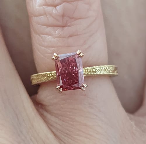 Close-up of a reviewer's solitaire carving engagement ring with a pink radiant-cut diamond on a detailed yellow gold band.