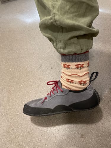 Reviewer's foot wearing one of the beige vintage flower socks with a gray cuff and a gray shoe.