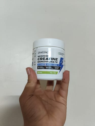Customer holding a white tub of Wellcore Micronised Creatine Monohydrate in the Kiwi Kick flavor.