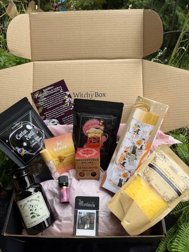 Kundenfoto der geöffneten Witchy Box Juli, das den Inhalt wie eine Kerze, Badesalz und andere Artikel auf rosa Seidenpapier zeigt.