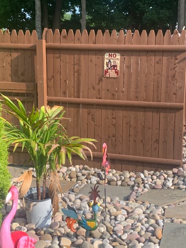 Customer's 'No Trespassing' personalized metal sign hanging on a brown wooden fence in a backyard.