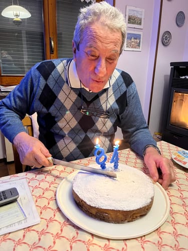 Il padre del recensore festeggia il suo 84° compleanno soffiando sulle candeline di una torta.