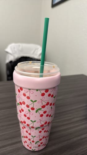 Customer's pink To-Go Buddy with a Cherry Crush pattern holding a drink cup with a green straw on a desk.