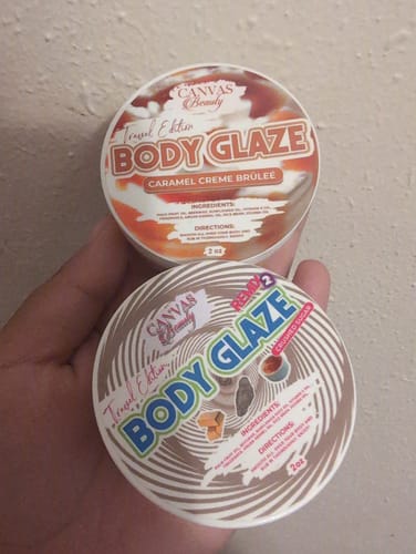 Customer's hand holding two round jars of Travel Glaze, with the Caramel Creme Brulee scent on top.