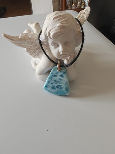 Pendentif en larimar d'un client, bleu comme un lagon, posé sur une figurine d'ange.