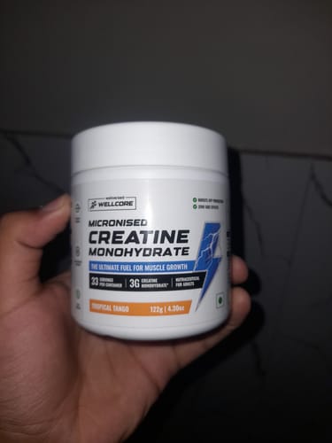 Customer's hand holding a white tub of Wellcore Micronised Creatine Monohydrate in Tropical Tango flavor.