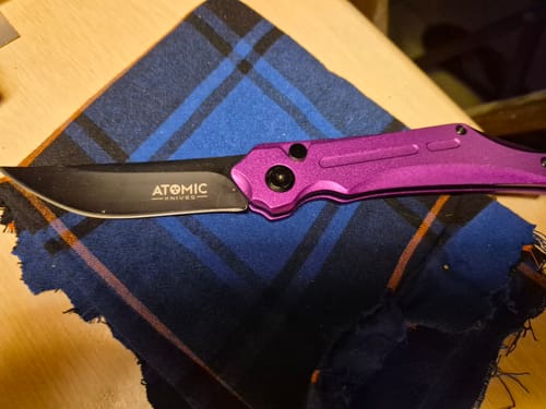 Customer's open Rogue Automatic Switchblade with a purple aluminum handle and black tanto blade, resting on a plaid cloth.