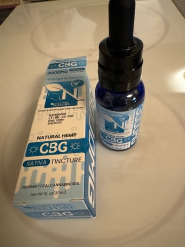 Customer's CBG Sativa Tincture in a blue bottle, standing next to its light blue box on a counter.