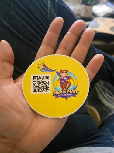 Customer holding a round, yellow custom vinyl sticker with a 'Mighty Minx' logo and a QR code.