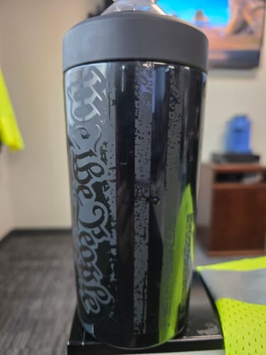 Customer's black Universal XL cooler with a distressed 'We The People' design holding a bottle on a desk.
