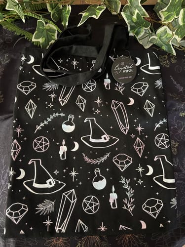 Rezensent zeigt die schwarze Crystal Witch Tasche flach ausgebreitet, umgeben von dekorativen Efeublättern.
