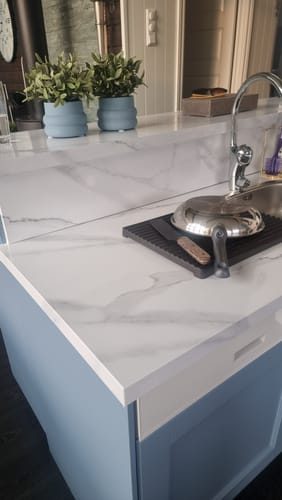 Kundens blå kjøkkenøy med benkeplate og bakvegg dekket av Marmor klassisk hvit kontaktplast.