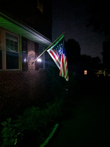 Reviewer's Solar Flagpole Light brightly illuminating a flag mounted on their house at night.