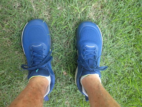 Customer standing on grass wearing blue CUURT Muuv court shoes, highlighting the wide toe box.