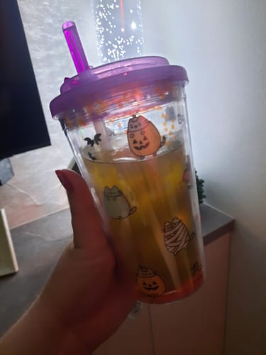 Ein Rezensent hält den gefüllten Spooky Pusheen Becher mit lila Deckel und Strohhalm in der Hand.