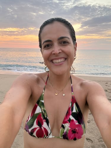 Reviewer smiling on a beach at sunset, wearing the gold Ellie® Chunky Bubble Huggies.