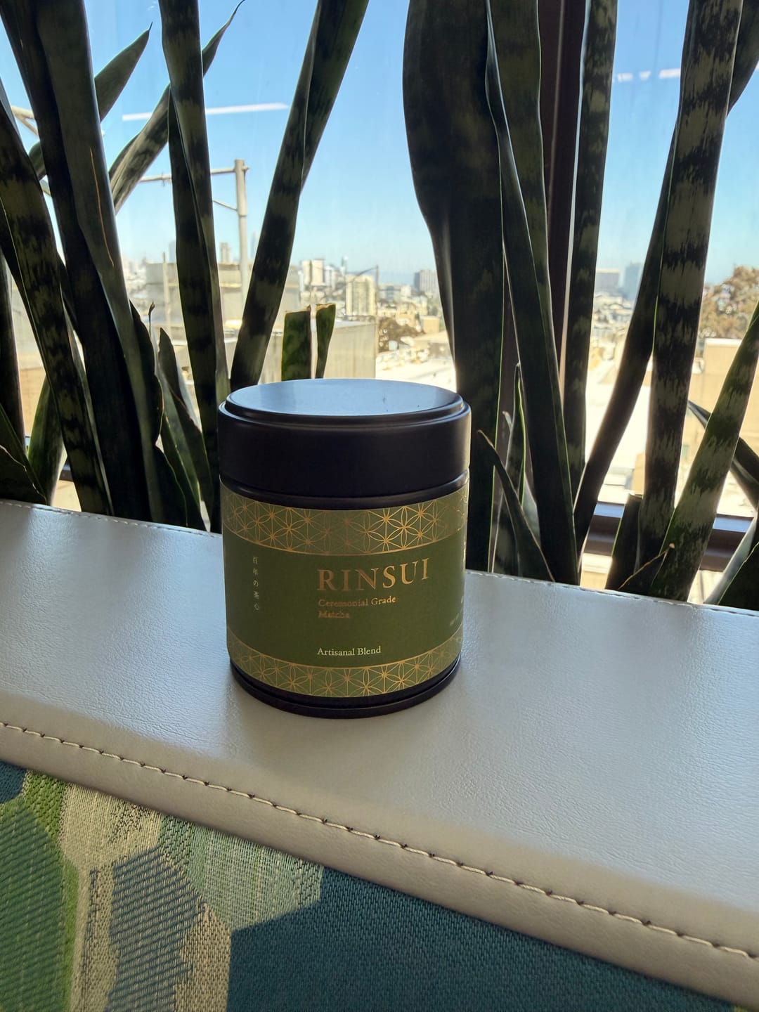 Customer's Artisanal Blend matcha tin by a window with a city view.