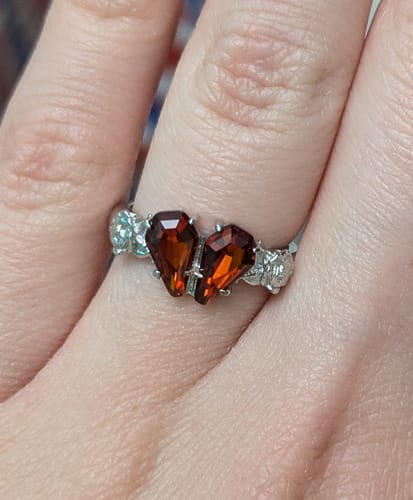 Customer's hand wearing the silver MINI PROMISE RING with two red, coffin-shaped stones.