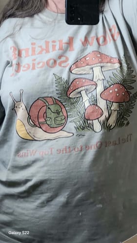 A customer wearing the light blue Slow Hiking Society Snail T-Shirt, showing the fit and the central graphic of a snail and mushrooms.