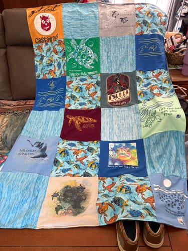 Customer's finished Project Repat T-Shirt Quilt with a vibrant turtle and ocean theme, draped over a couch.