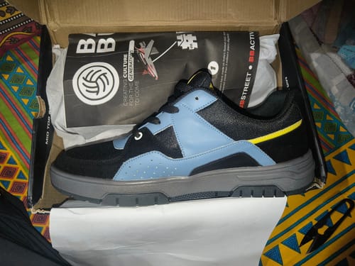 Customer's new GROOVE sneaker in black and blue, shown from the side inside its open box.