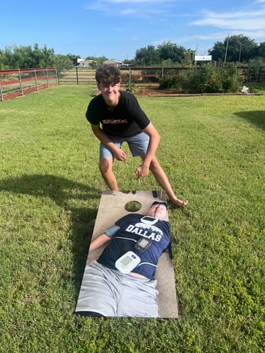 Customer pointing at a custom cornhole board wrap featuring a funny photo of a person, set up in a grassy yard.