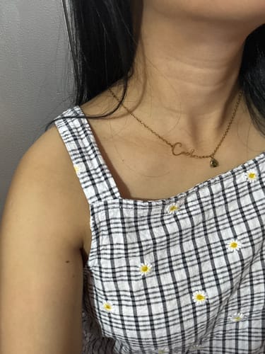 A customer wearing the Lucce Signature Necklace, showing the gold-tone script name and teardrop stone.