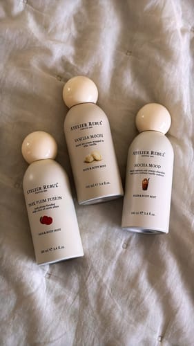 Customer's Vanilla Mochi Hair & Body Mist, placed with two other scents from the collection on a white, quilted surface.