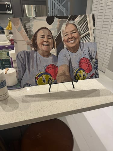 Customer's completed Custom Paint By Numbers portrait of two women displayed on an easel on a counter.