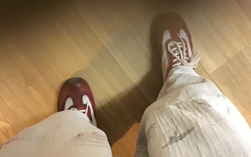 Reviewer's first-person view of the red and white colorblock leather sport shoes on a wood floor.