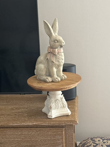 Customer's Léon French Provincial Cake Stand in antique white, displaying a decorative rabbit figurine on its fir wood top.