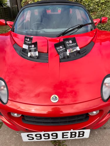 Reviewer's packets of Dutch Black Salty Liquorice Mix displayed on the bonnet of their red sports car.