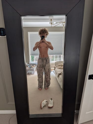 Reviewer in a mirror selfie showing the baggy fit of the Heritage Camo Cargo Sweats in a bedroom.