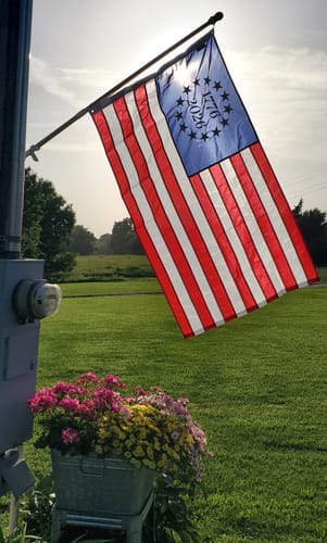 Customer's 1776 to 2026 Betsy Ross Flag flying on a pole outside, backlit by the bright sun.