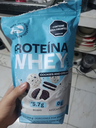 Un cliente sostiene la bolsa de Proteína Whey sabor Cookies & Cream en su mano, mostrando la parte frontal del producto.