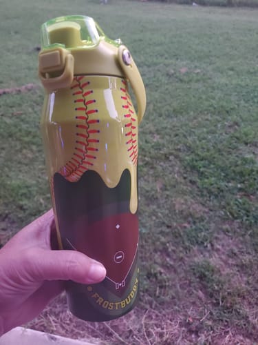 Reviewer holding their Bottle Buddy with the Softball Drip design outdoors in a grassy area.