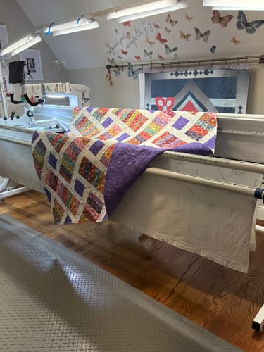 Reviewer's finished Crazy Daisy quilt top, with a colorful pattern and purple backing, draped over a quilting machine.