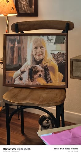 Reviewer's completed custom painting of a person and a dog, framed and resting on a chair.