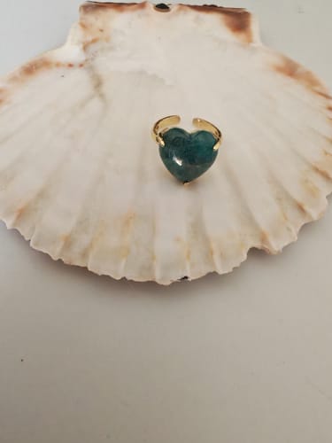 Bague Apatite d'un client, avec sa pierre en forme de cœur, posée dans un coquillage blanc.